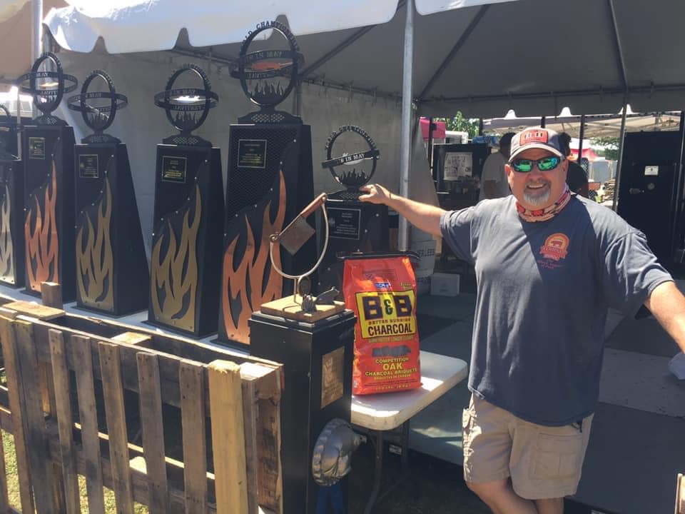 Pitmaster showcasing Yoder smokers and BBQ supplies at a grilling event, featuring charcoal and accessories.