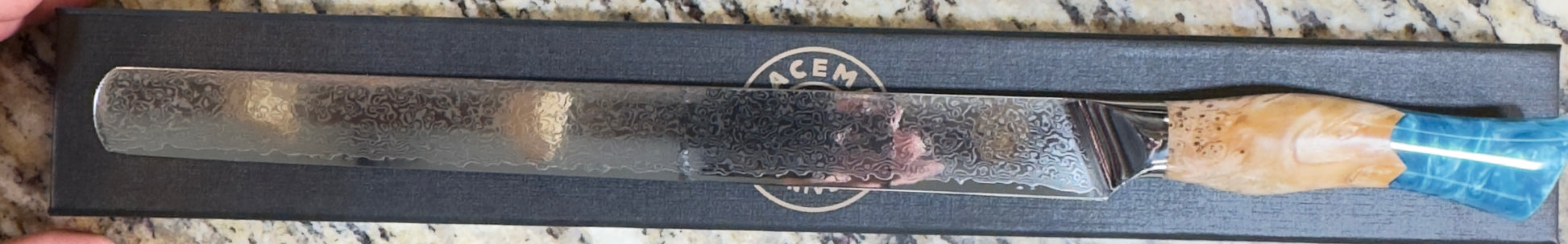 Spaceman Knives Brisket Slicer displayed on a box, featuring a 12-inch Damascus blade and blue epoxy handle.