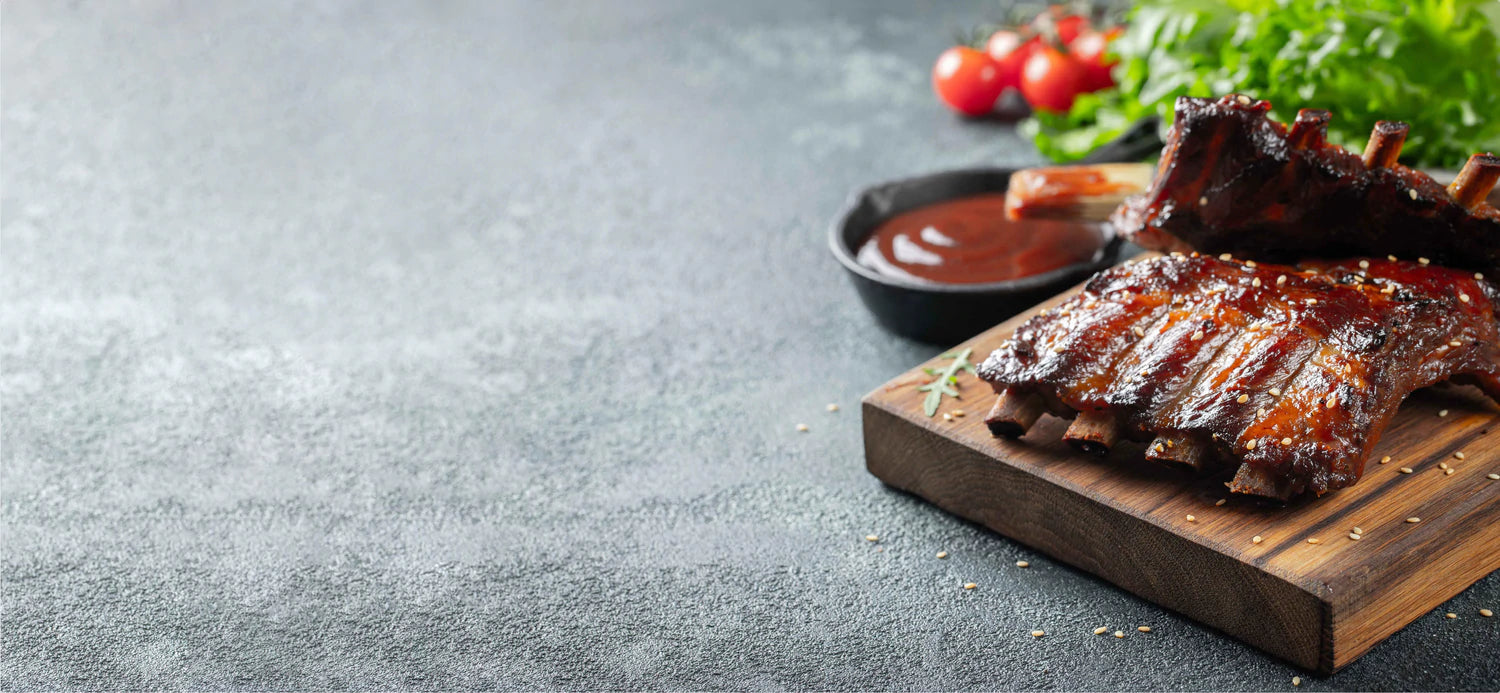 Delicious BBQ ribs with sauce, fresh tomatoes, and greens on a wooden cutting board, perfect for grilling enthusiasts.