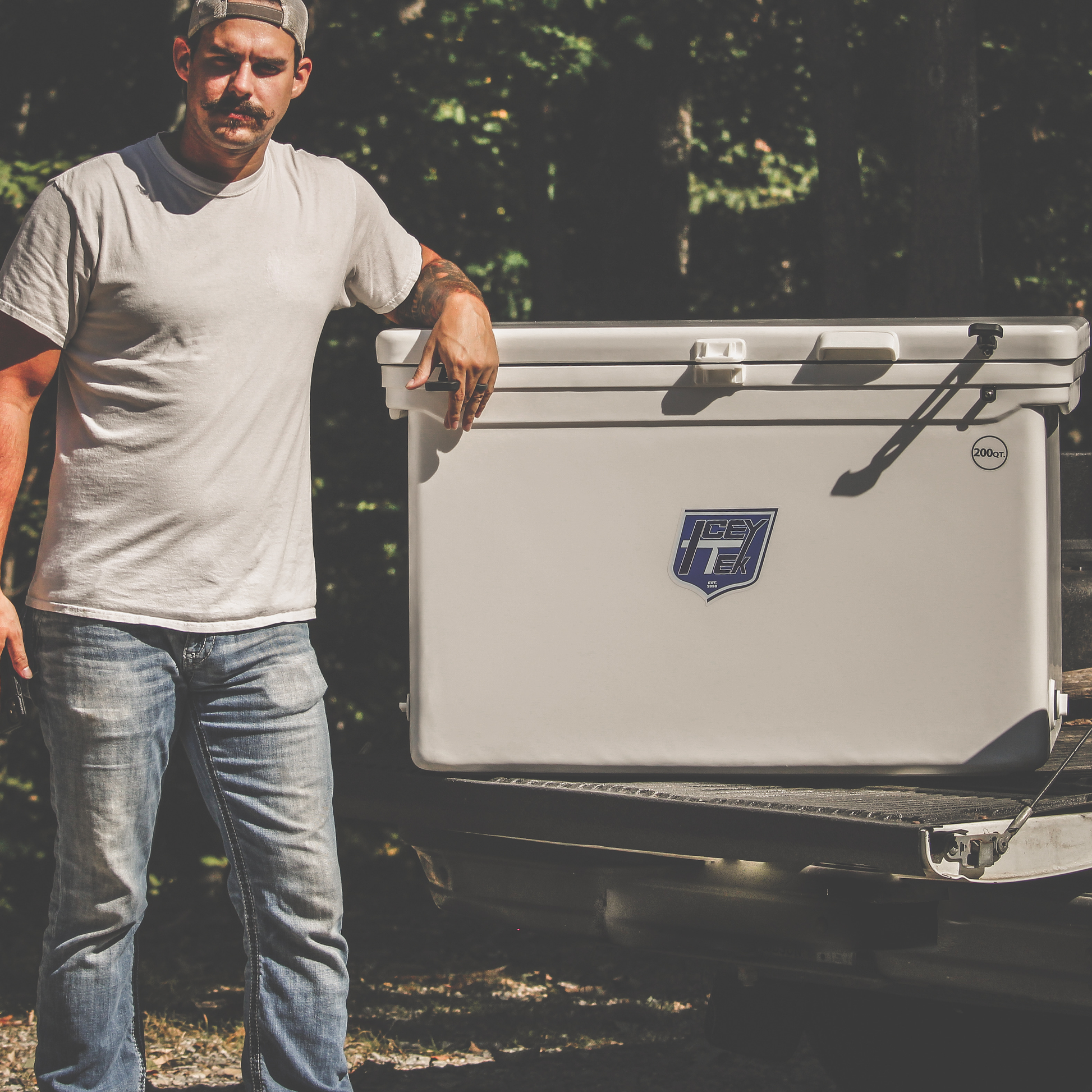 Man beside ICEY-TEK 200 Quart Cooler (FREE SHIPPING) on truck, showcasing its rugged design for outdoor adventures.