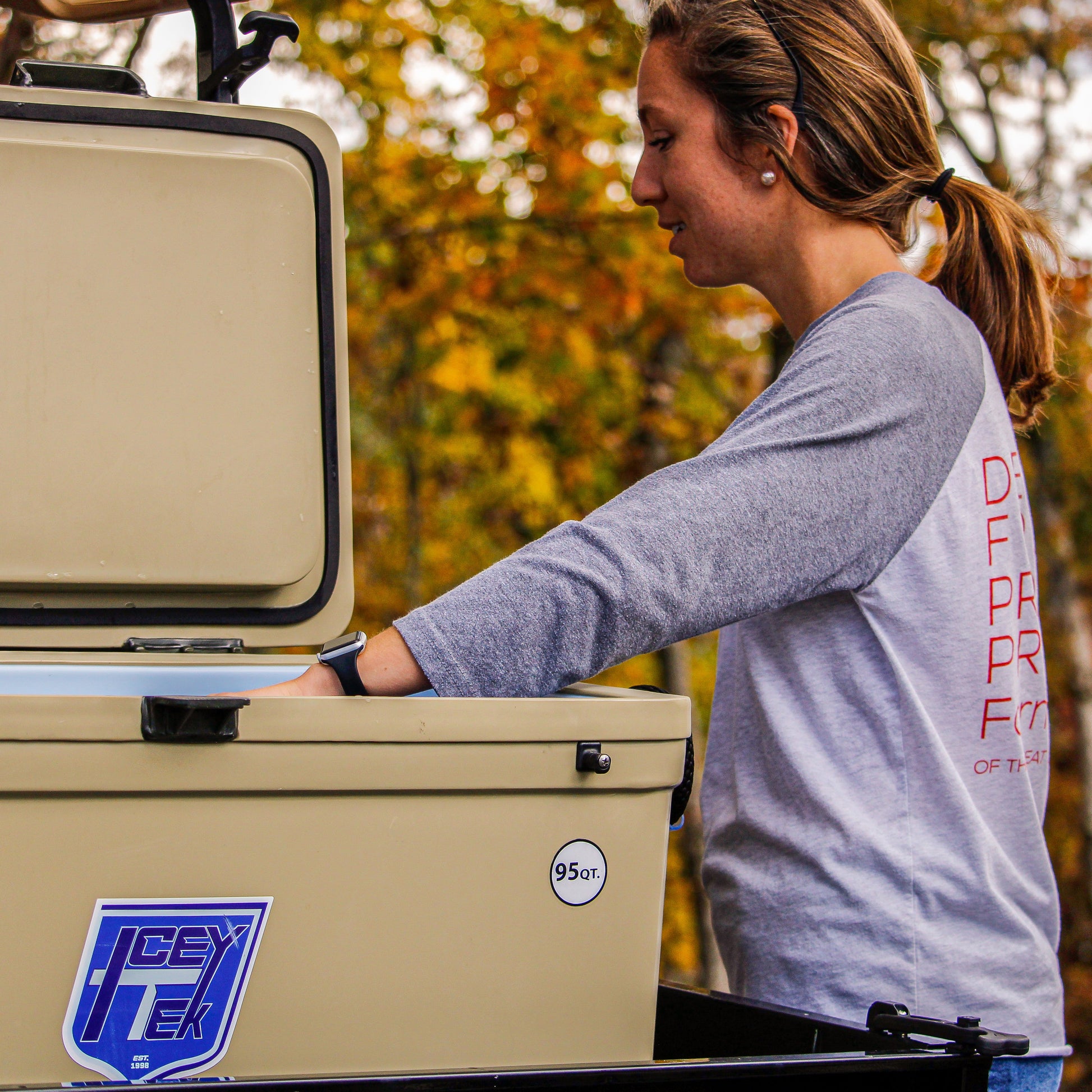 Woman using the ICEY-TEK 95 Quart Cooler (FREE SHIPPING) outdoors, showcasing its rugged design and functionality.
