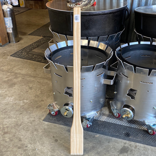 Cajun Classic Wooden Mixing Paddle next to outdoor grills and cookers, perfect for BBQ enthusiasts and grilling tools.