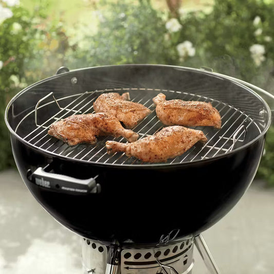 Seasoned chicken quarters cooking on a black charcoal kettle grill