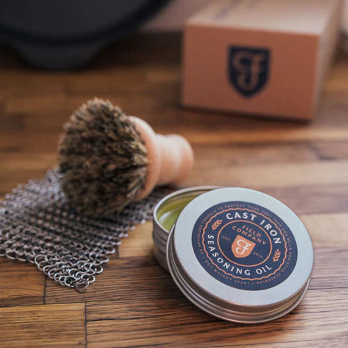 Field Company Cast Iron Care Kit including seasoning oil, natural fiber brush, and chain mail scrubber for grill maintenance.