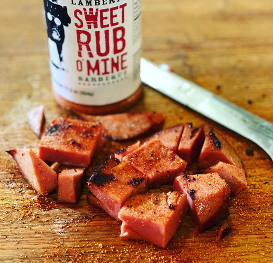 Sliced BBQ meat seasoned with Lambert's Sweet Rub o' Mine on a wooden cutting board, showcasing BBQ flavors.