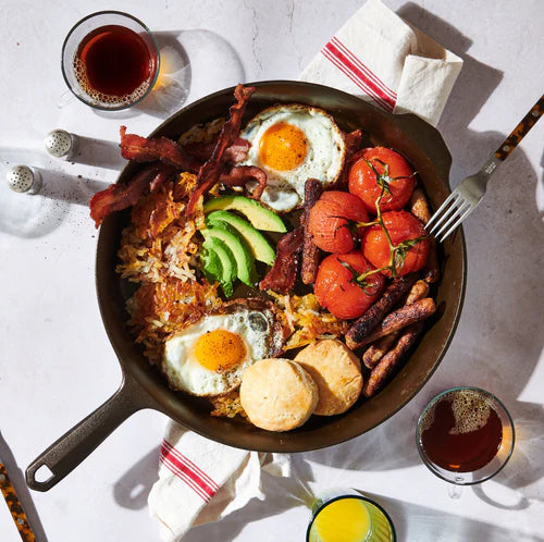 Field Company No. 12 Cast Iron Skillet with breakfast, eggs, bacon, tomatoes, and avocado on a table.