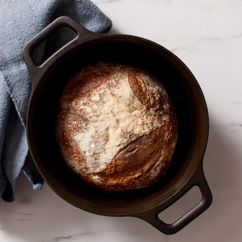 Freshly baked bread in a Field Company No.8 Cast Iron Dutch Oven on a marble countertop.