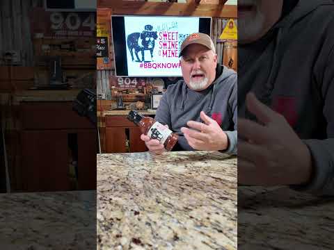 Person showcasing Sweet Sauce O' Mine Original 18 oz. with barbecue setup, highlighting BBQ lifestyle and cooking tools.